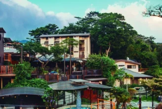 Hotel Poco a Poco Monteverde exterior showing the indoor heated pool, tropical gardens, and mountain backdrop.